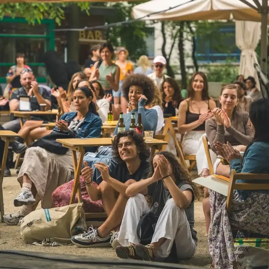 Grupa osób siedzących na zewnątrz na tarasie, klaszczących podczas przyjaznego spotkania w kawiarni.